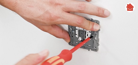 Mains vissant une prise électrique murale avec tournevis rouge