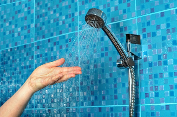 Main sous un pommeau de douche noir avec eau qui coule