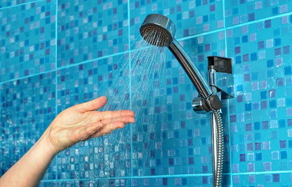 Main sous un pommeau de douche noir avec eau qui coule