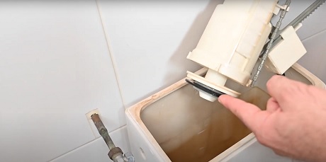 Main montrant l'intérieur rouillé d'un réservoir de toilettes ouvert