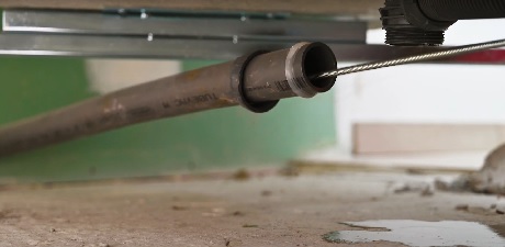 Tuyau métallique corrodé sous un meuble avec traces d'humidité