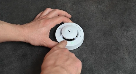 Mains tenant un détecteur de fumée rond gris