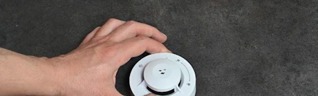 Mains tenant un détecteur de fumée rond gris