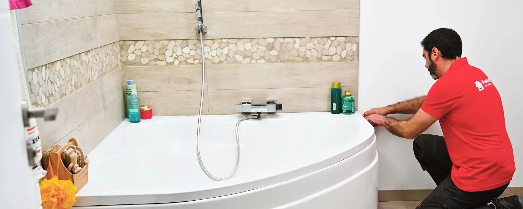 Technicien en rouge inspectant une baignoire d'angle dans salle de bain carrelée