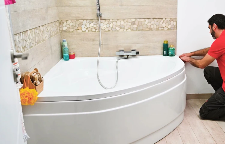 Technicien en rouge inspectant une baignoire d'angle dans salle de bain carrelée