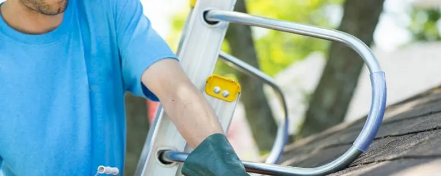 Homme nettoyant une gouttière depuis une échelle avec un seau orange