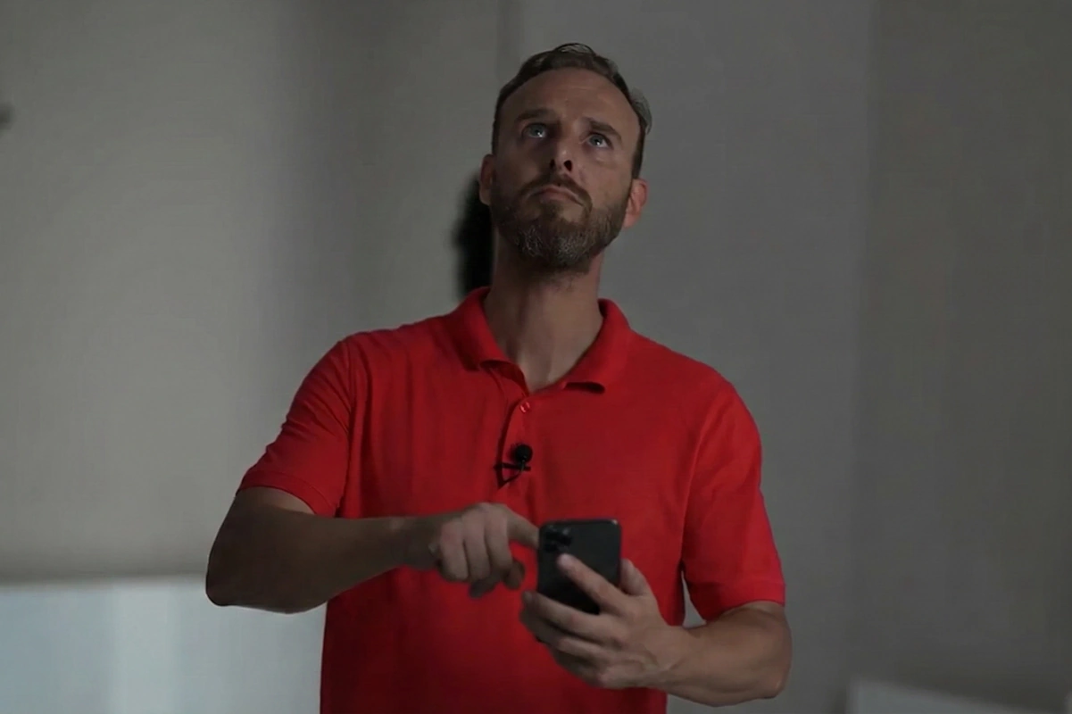 Homme en polo rouge tenant un téléphone et regardant vers le haut