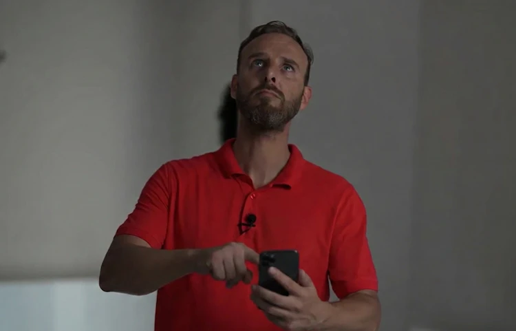 Homme en polo rouge tenant un téléphone et regardant vers le haut