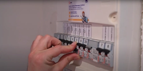 Main manipulant un disjoncteur sur un tableau électrique avec étiquettes