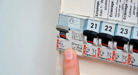Doigt appuyant sur un disjoncteur dans un tableau électrique