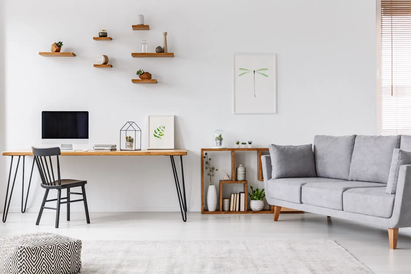 Salon lumineux avec canapé gris, bureau en bois et étagères murales