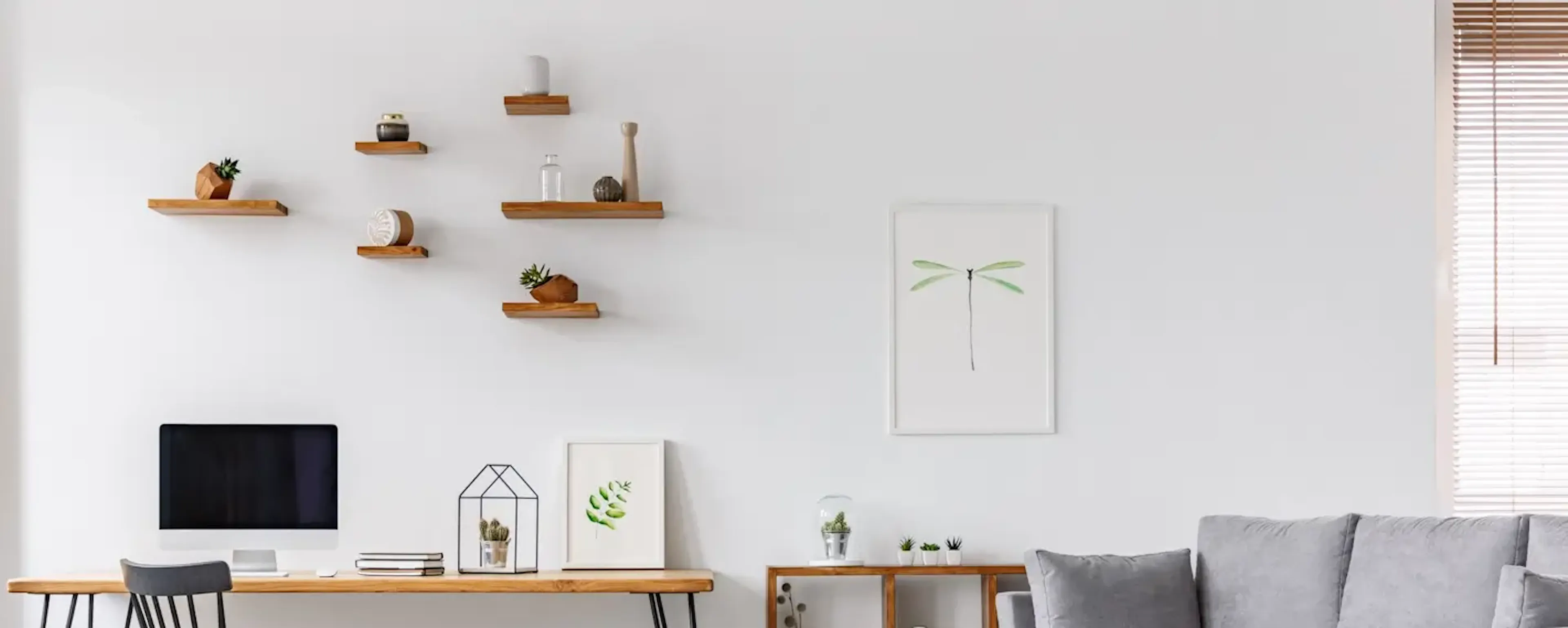 Salon lumineux avec canapé gris, bureau en bois et étagères murales