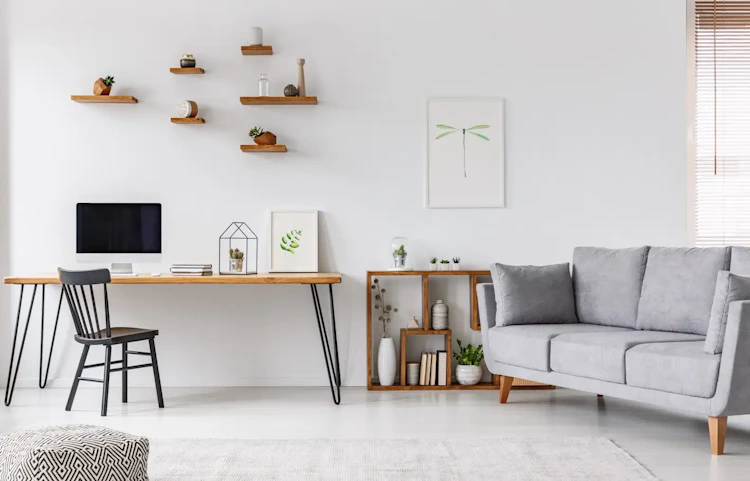 Salon lumineux avec canapé gris, bureau en bois et étagères murales