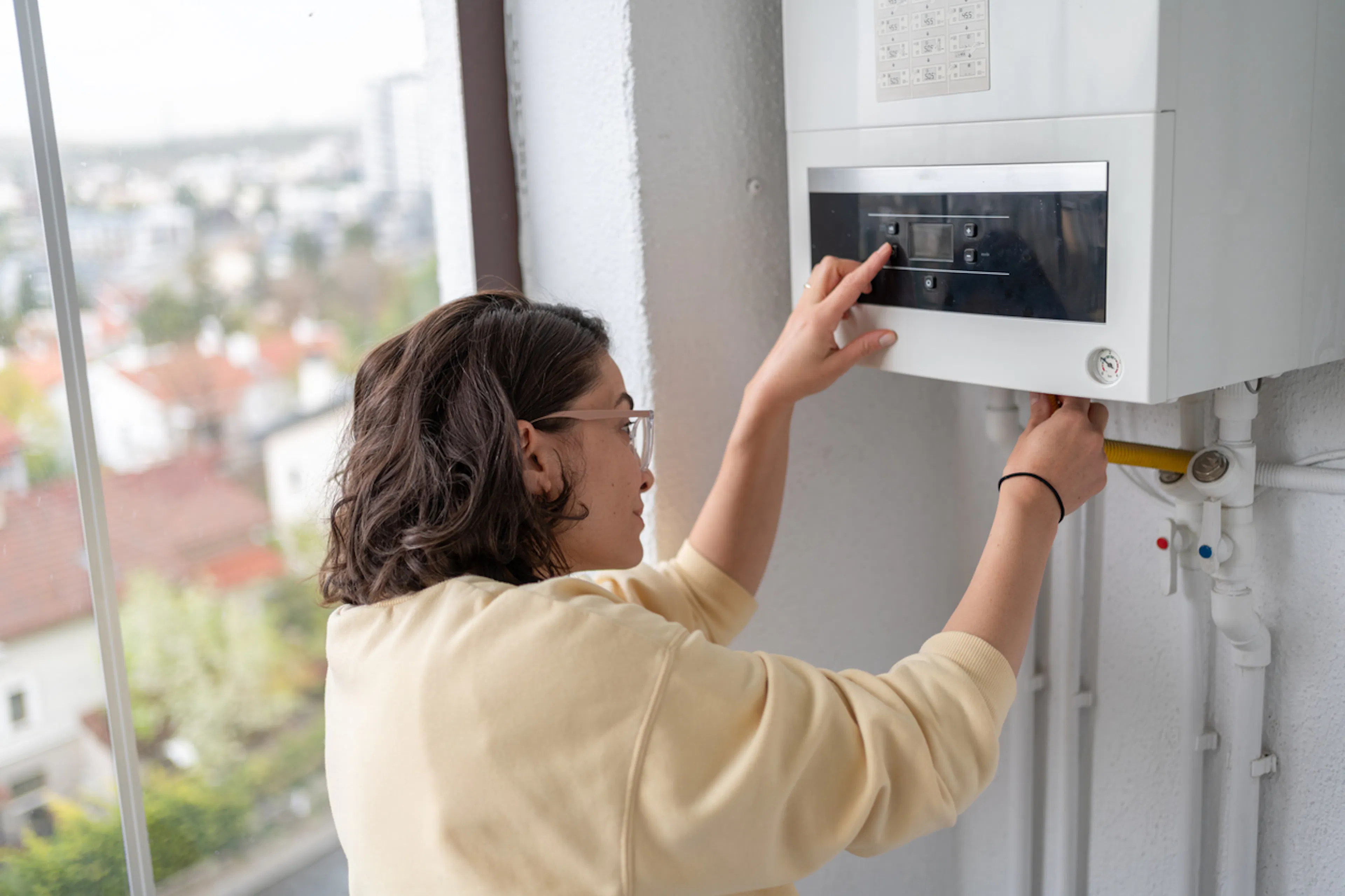 Femme ajustant la pression et les réglages de sa chaudière gaz dans son appartement suite à une augmentation du prix du gaz