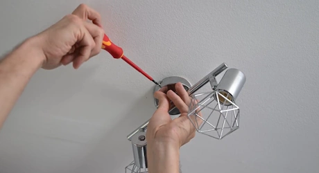 Mains vissant une applique murale métallique avec tournevis rouge