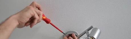 Mains vissant une applique murale métallique avec tournevis rouge