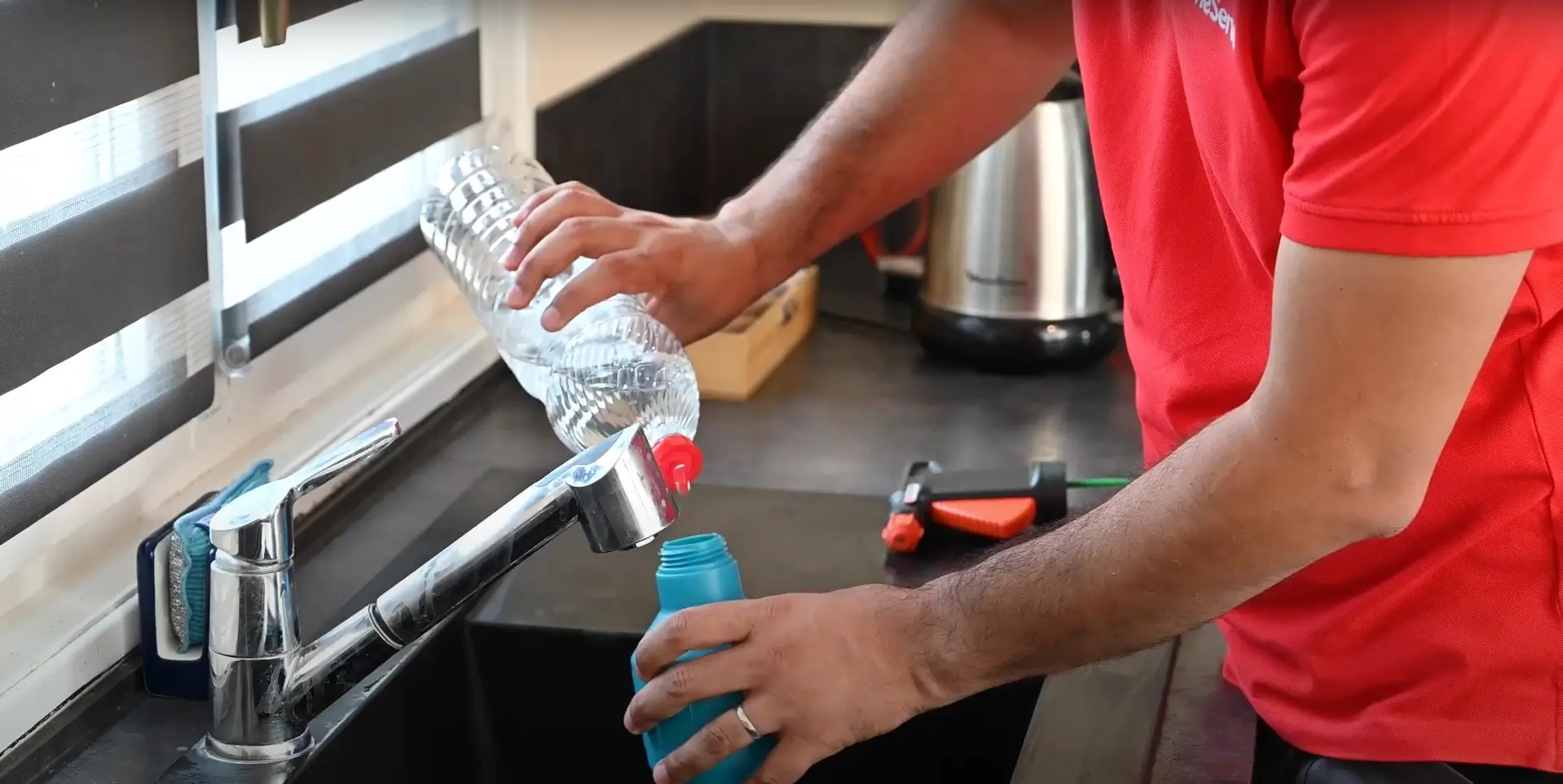 Homme en rouge remplissant une bouteille d'eau au robinet de cuisine