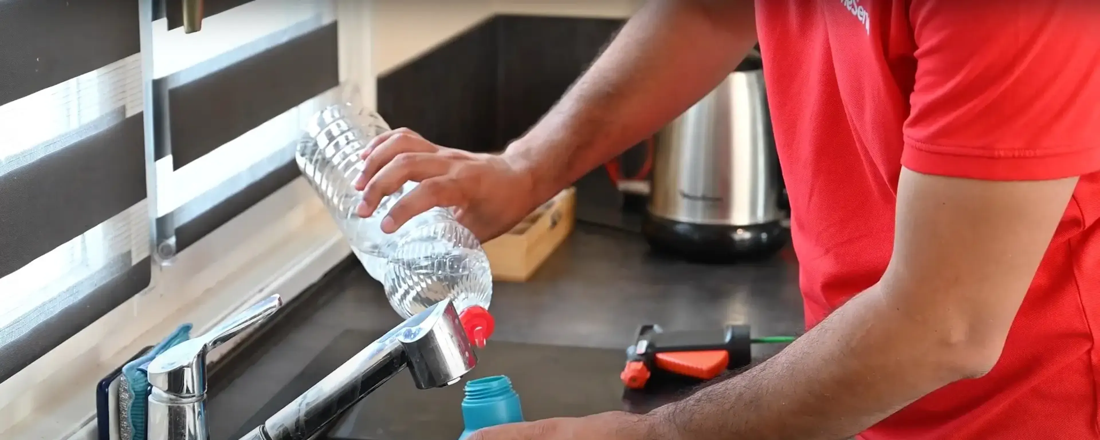 Homme en rouge remplissant une bouteille d'eau au robinet de cuisine