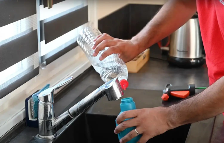 Homme en rouge remplissant une bouteille d'eau au robinet de cuisine