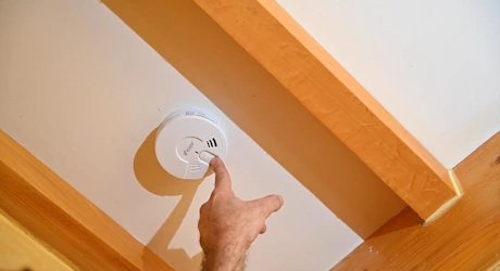 Main appuyant sur le bouton test d'un détecteur de fumée au plafond
