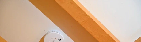 Main appuyant sur le bouton test d'un détecteur de fumée au plafond