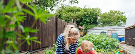 Mère et enfant jardinent ensemble dans un potager avec brouette verte