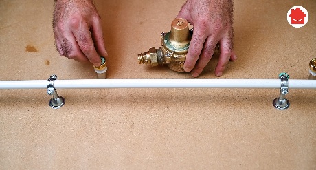 Deux mains installant un réducteur de pression laiton sur une canalisation