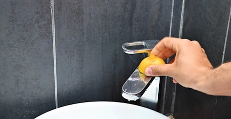 Main frottant un robinet avec un citron et du bicarbonate