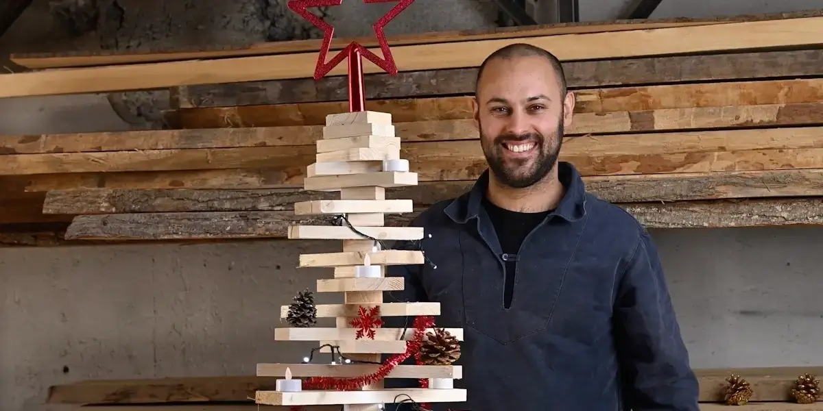 Homme souriant posant devant un sapin de Noël fait de planches en bois