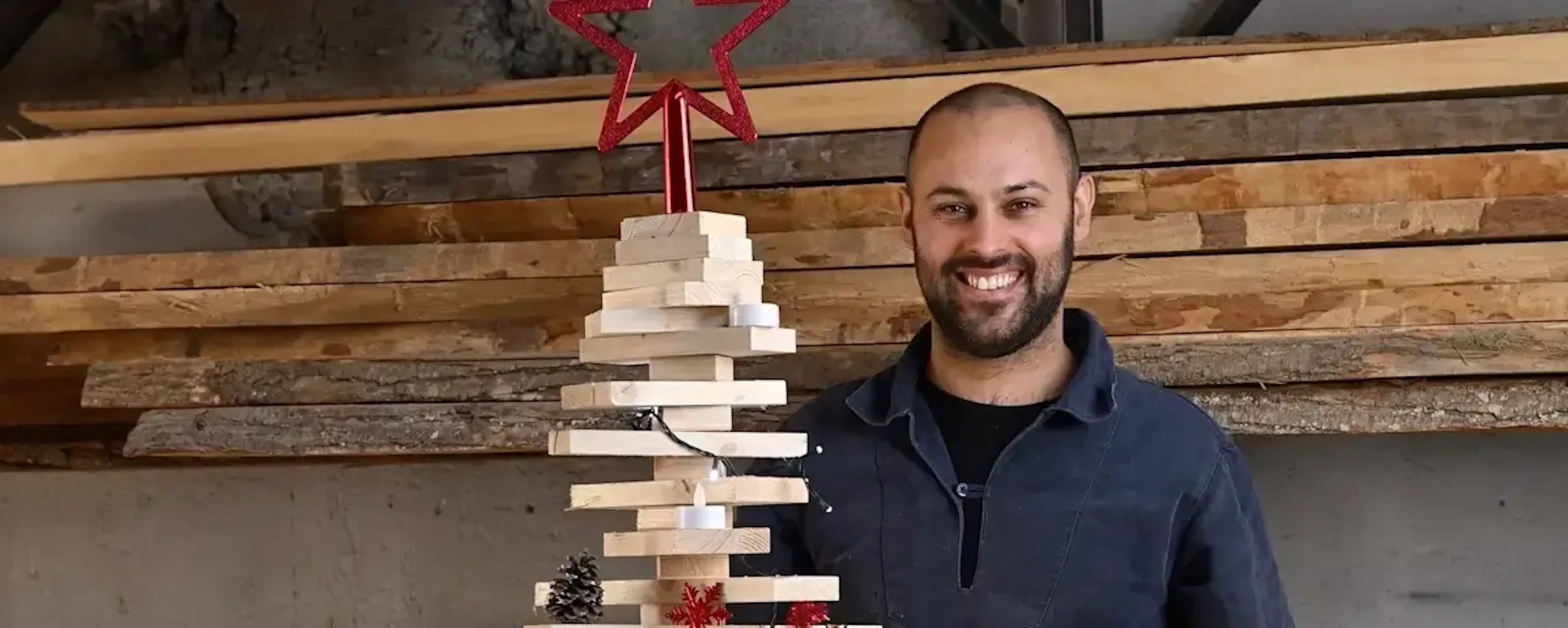 Homme souriant posant devant un sapin de Noël fait de planches en bois