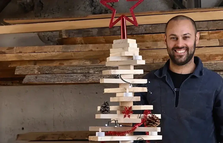 Homme souriant posant devant un sapin de Noël fait de planches en bois