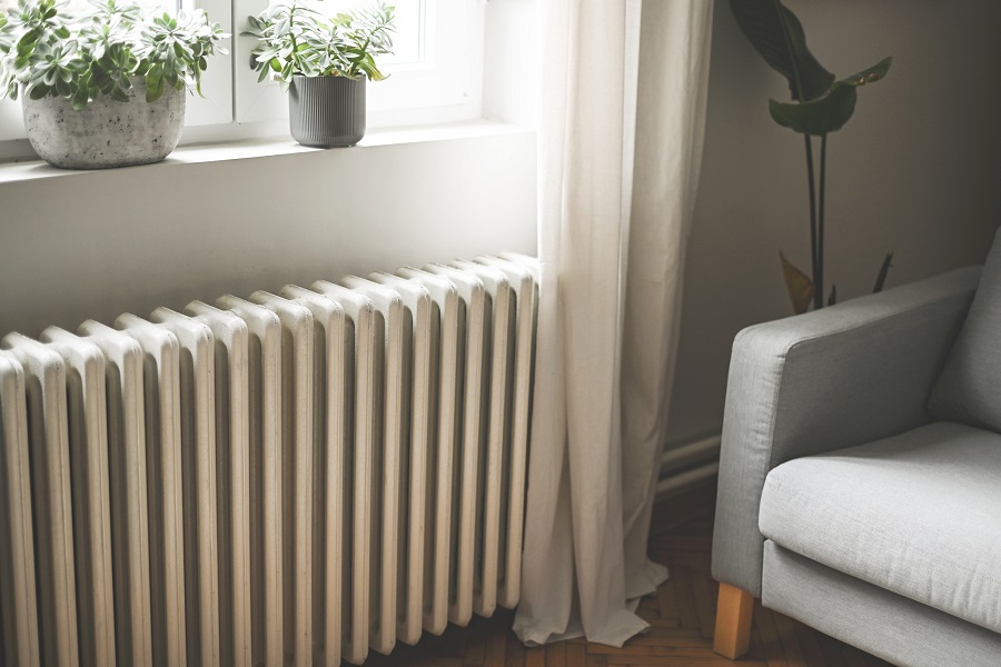 Radiateur blanc sous une fenêtre avec plantes et fauteuil gris