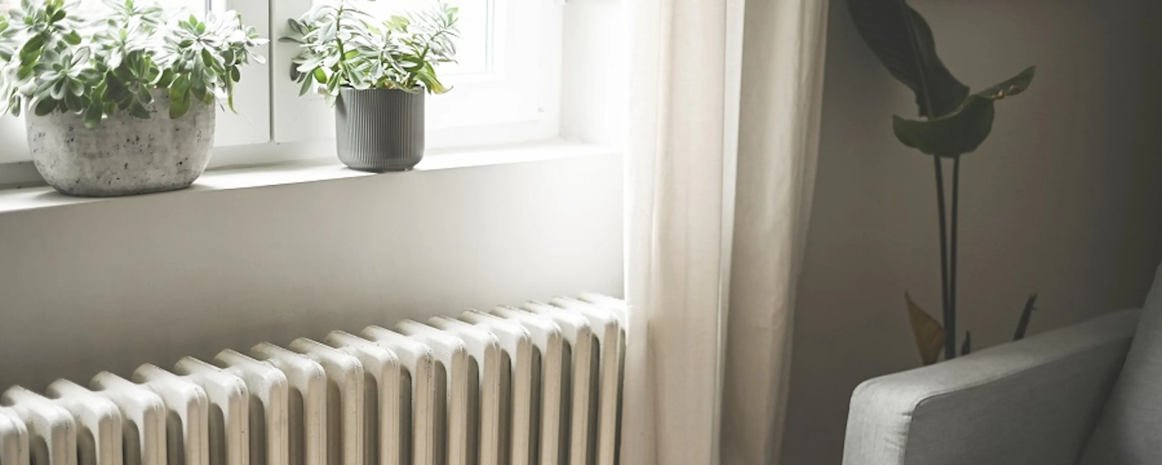 Radiateur blanc sous une fenêtre avec plantes et fauteuil gris