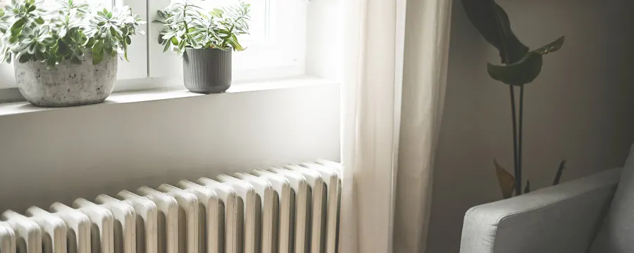 Radiateur blanc sous une fenêtre avec plantes et fauteuil gris