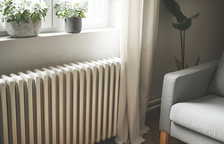Radiateur blanc sous une fenêtre avec plantes et fauteuil gris