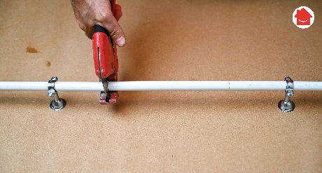 Main utilisant un coupe-tube rouge pour couper un tuyau blanc