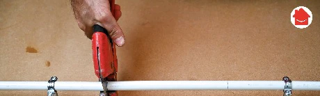 Main utilisant un coupe-tube rouge pour couper un tuyau blanc