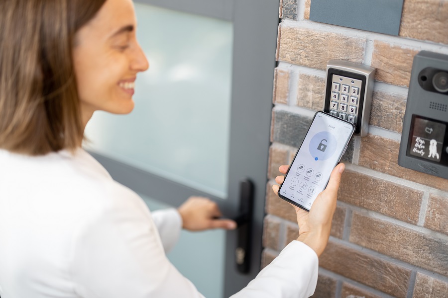 Femme utilisant son smartphone devant un digicode d'entrée sécurisé
