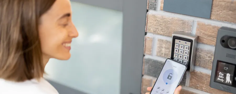 Femme utilisant son smartphone devant un digicode d'entrée sécurisé
