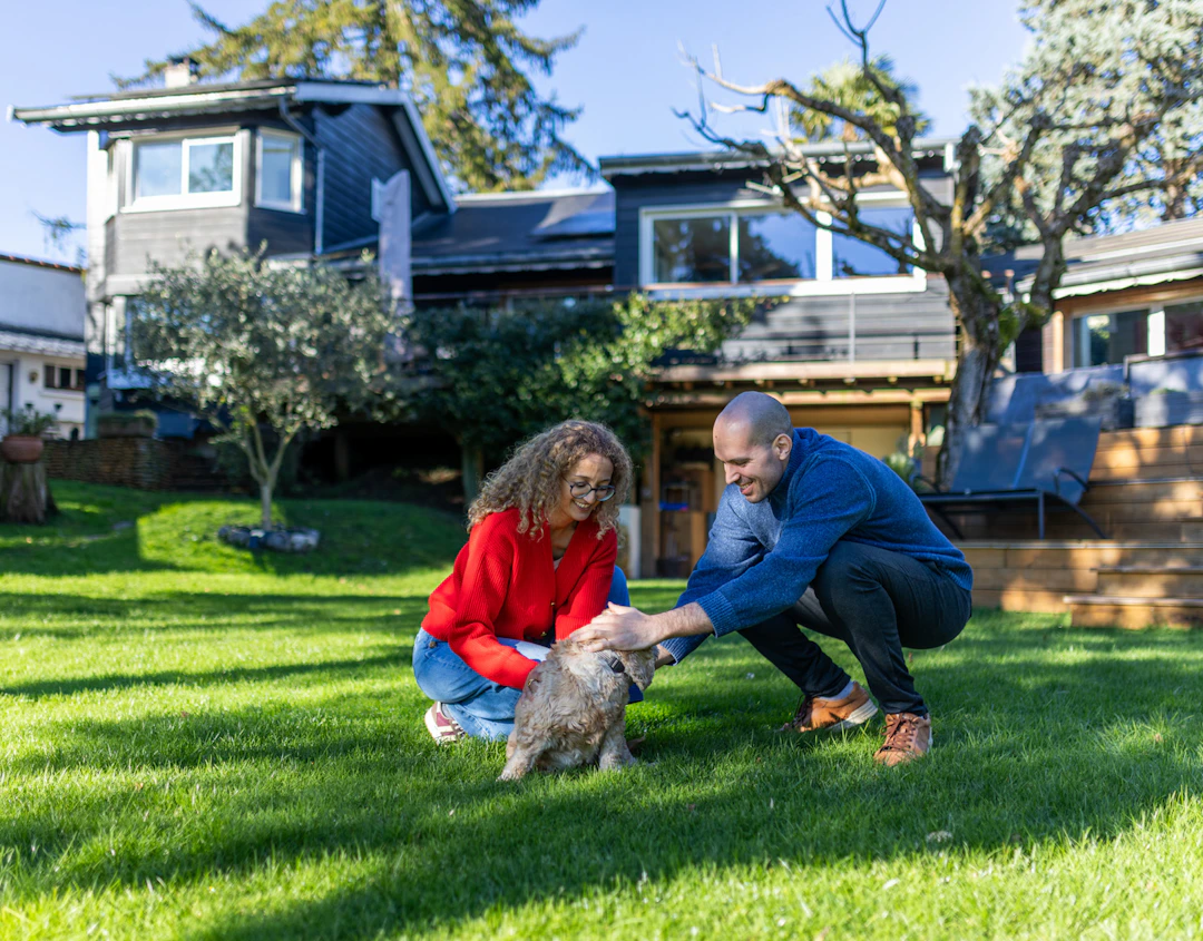 Un couple et leur chien dans leur jardin, devant leur maison rénovée par HomeServe