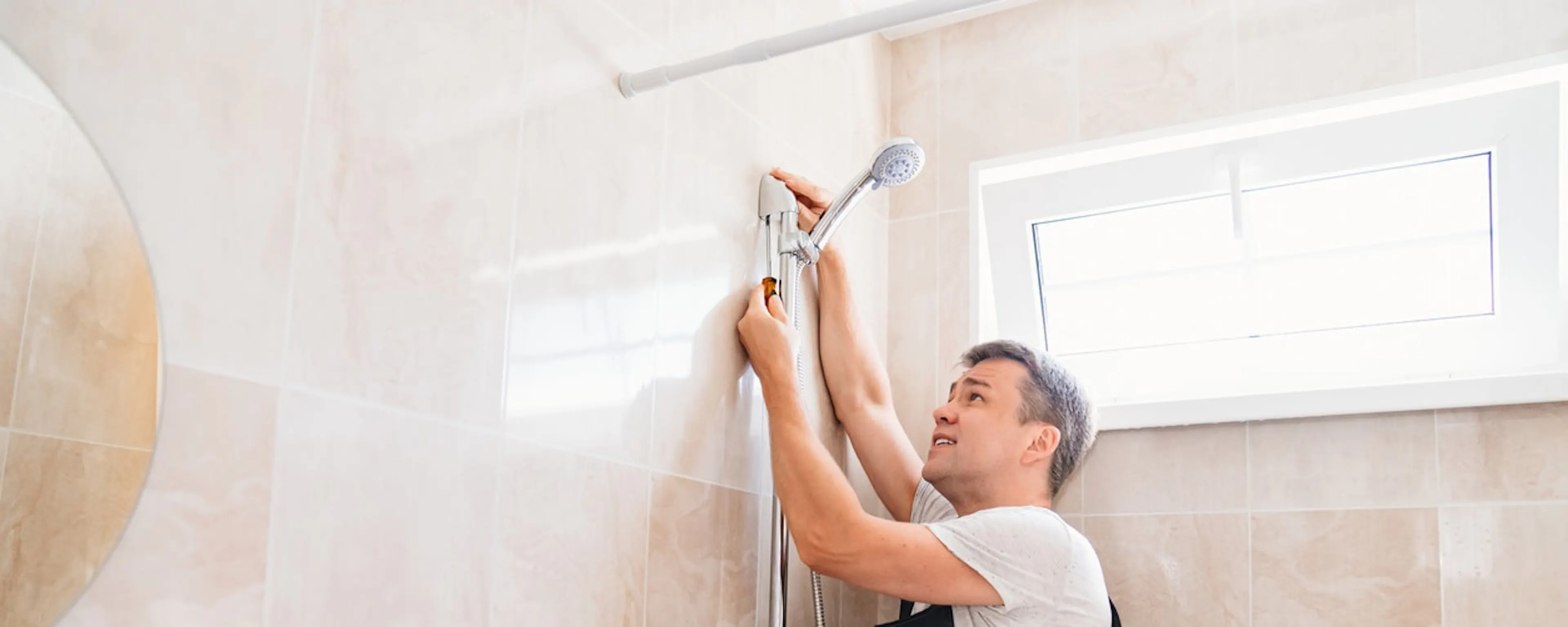 Plombier installant une colonne de douche sur un mur carrelé beige