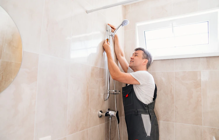 Plombier installant une colonne de douche sur un mur carrelé beige