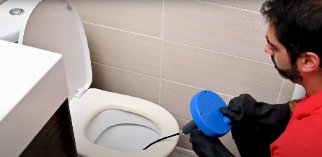 Homme avec furet électrique débouchant des toilettes dans une salle de bain