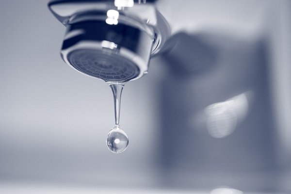 Robinet chromé avec une goutte d'eau tombant, fond bleu