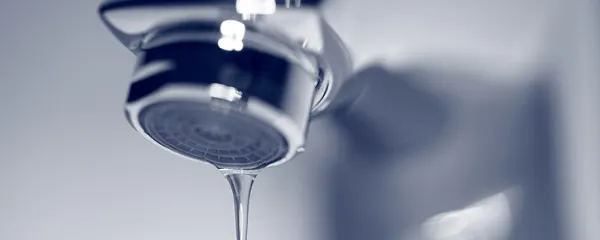 Robinet chromé avec une goutte d'eau tombant, fond bleu