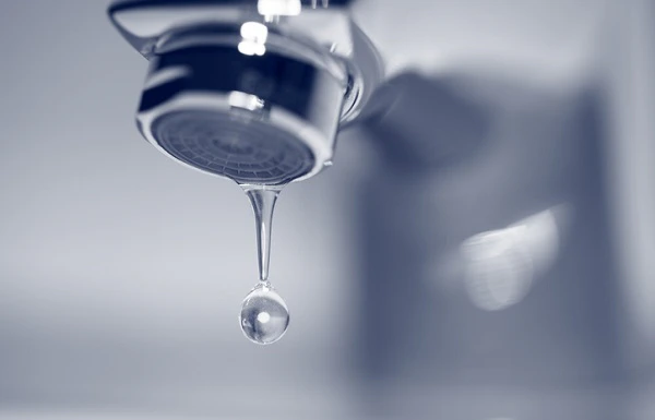 Robinet chromé avec une goutte d'eau tombant, fond bleu
