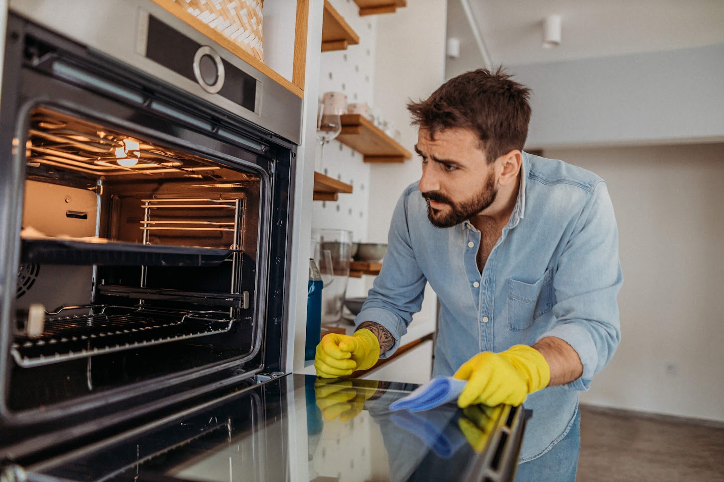 Homme nettoyant la vitre d'un four avec des gants jaunes