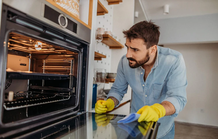 Homme nettoyant la vitre d'un four avec des gants jaunes