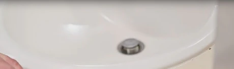 Main grattant l'ancien joint silicone autour d'un lavabo avec un outil noir