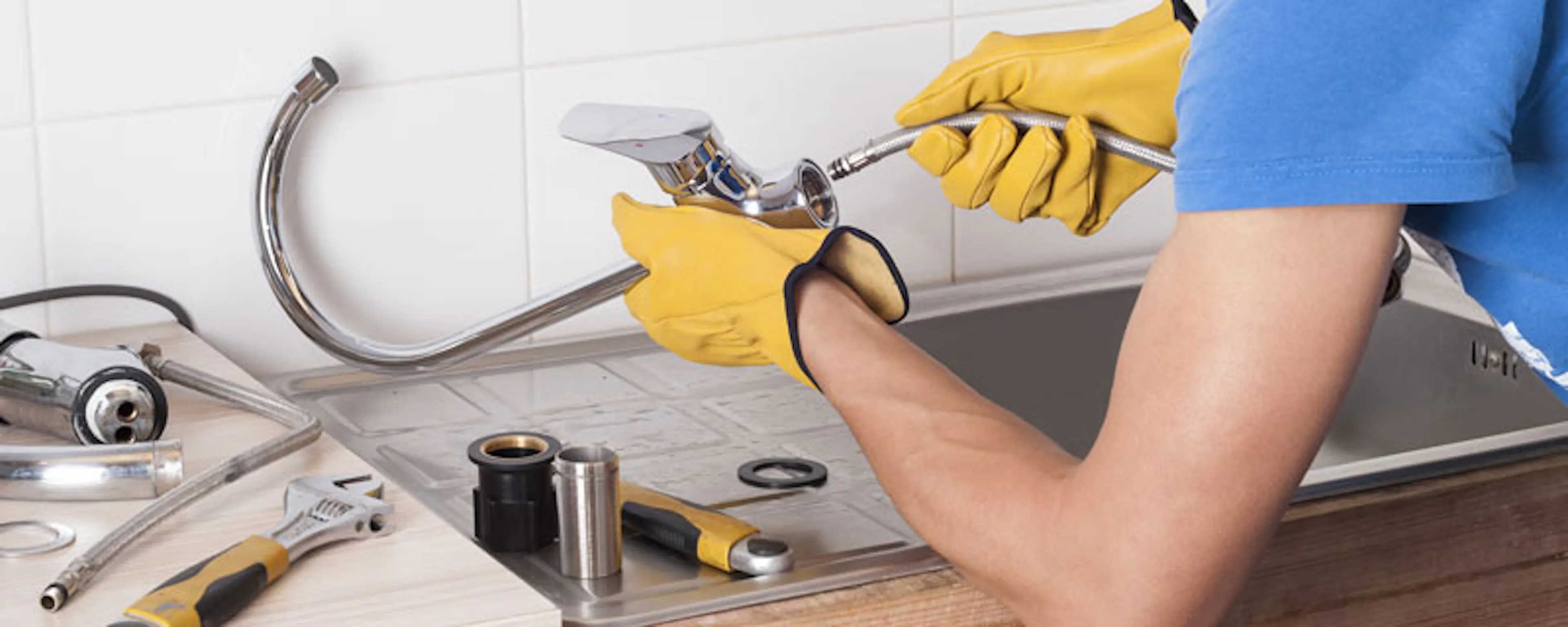 Plombier avec gants jaunes réparant une tuyauterie sous évier